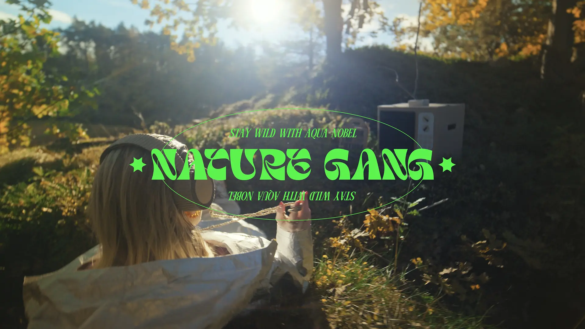 Grafiken Nature Gang – Stay wild with Aqua Nobel över en solig skogsbild